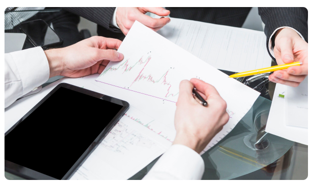 Two colleagues reviewing a hand-drawn financial chart with a tablet and pen on a glass table